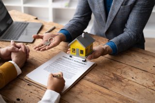 Reliable real estate agent giving keys to couple, male female hands close up receiving the house keys after the dealing.